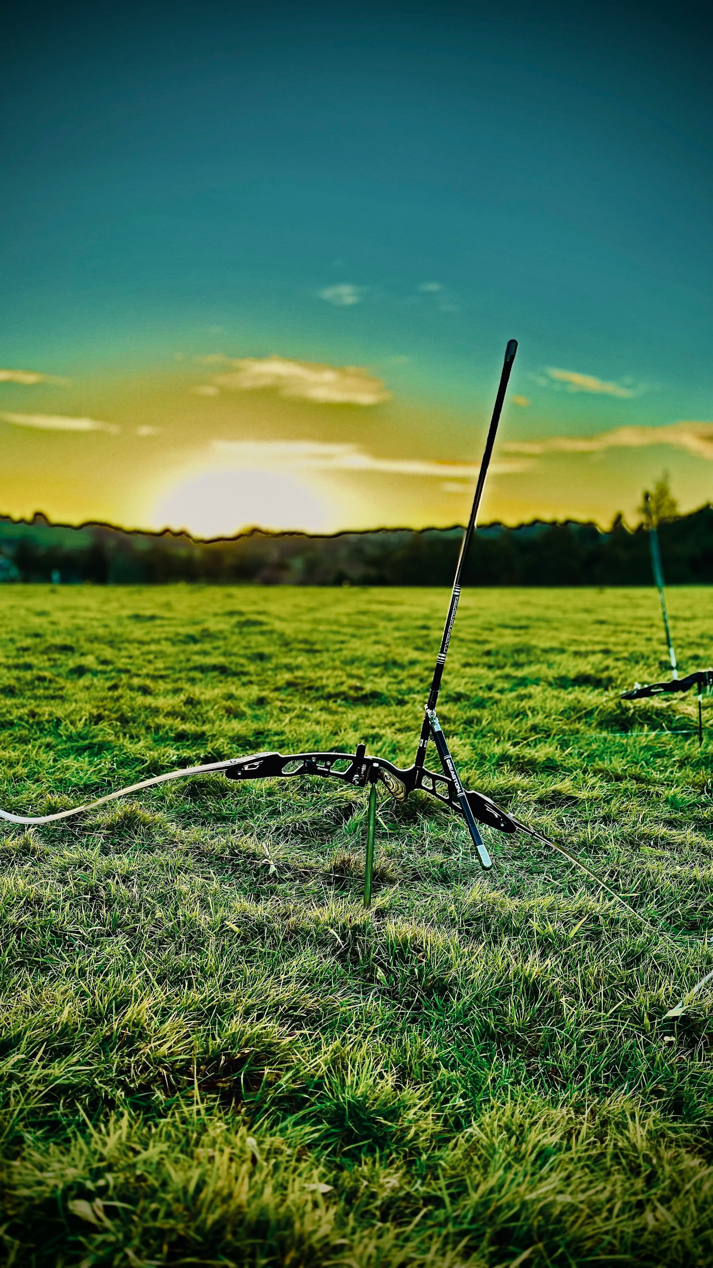 A recurve archery bow resting on a grassy field at sunset. Target your technology strategy.